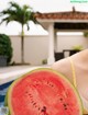 A woman holding a slice of watermelon in front of a pool.