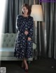 A woman in a blue dress standing in front of a couch.