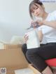 A woman sitting on top of a cardboard box holding a pair of scissors.