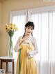 A woman in a yellow and white dress standing in front of a window.