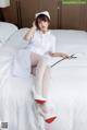 A woman in a white nurse outfit sitting on a bed.