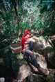 A woman in a red hoodie sitting on a rock in the woods.