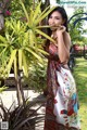 A woman in a long dress standing next to a tree.